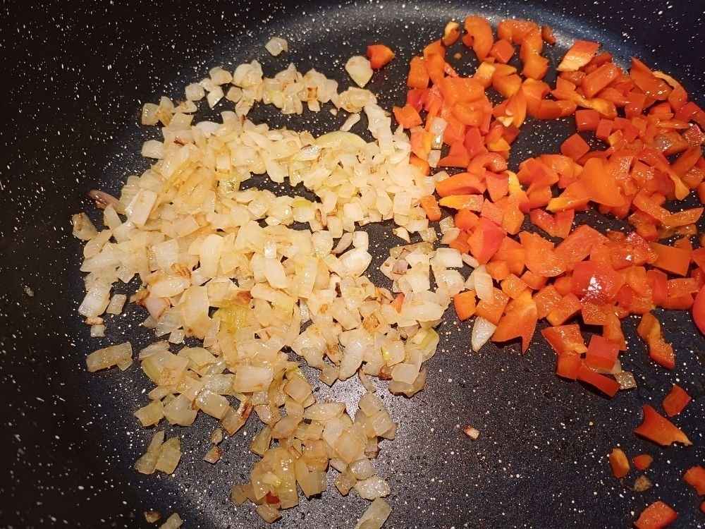 Sauteed onions and red pepper on a frying pan