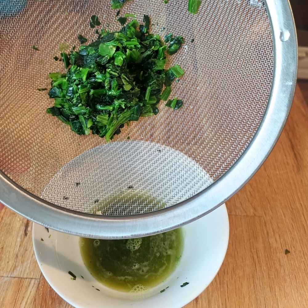 Frozen spinach in a sieve being drained from excess water into a ceramic bowl