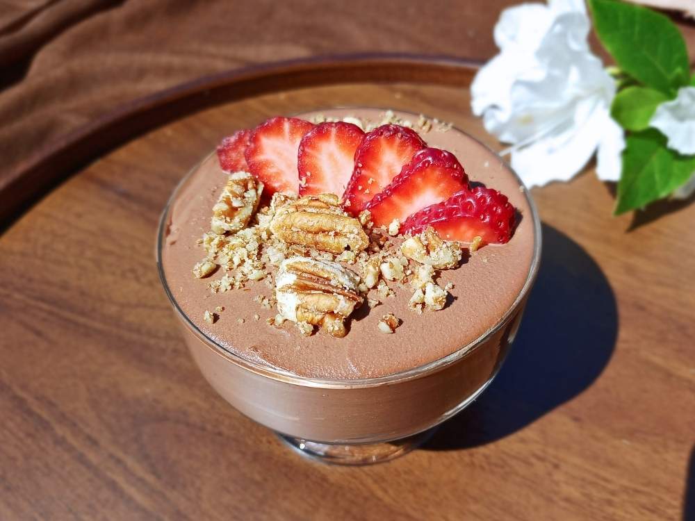 Cottage cheese chocolate mousse in a glass serving cup with white flowers in the background.