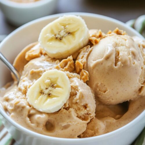 Banana Peanut protein Ninja creami ice cream scoops in a white bowl with slices of banana on top