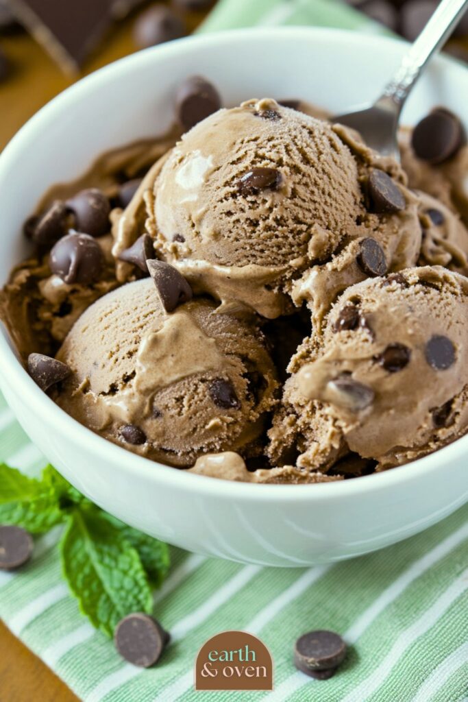 A bowl of chocolate mint Ninja Creami Protein ice cream with chocolate chips on a green striped cloth on a wooden table.