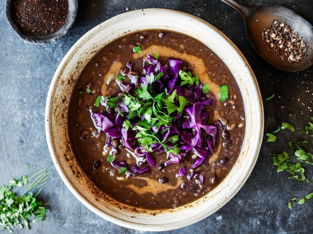 A bowl of fresh black bean soup with purple cabbage and fresh green herbs on top.