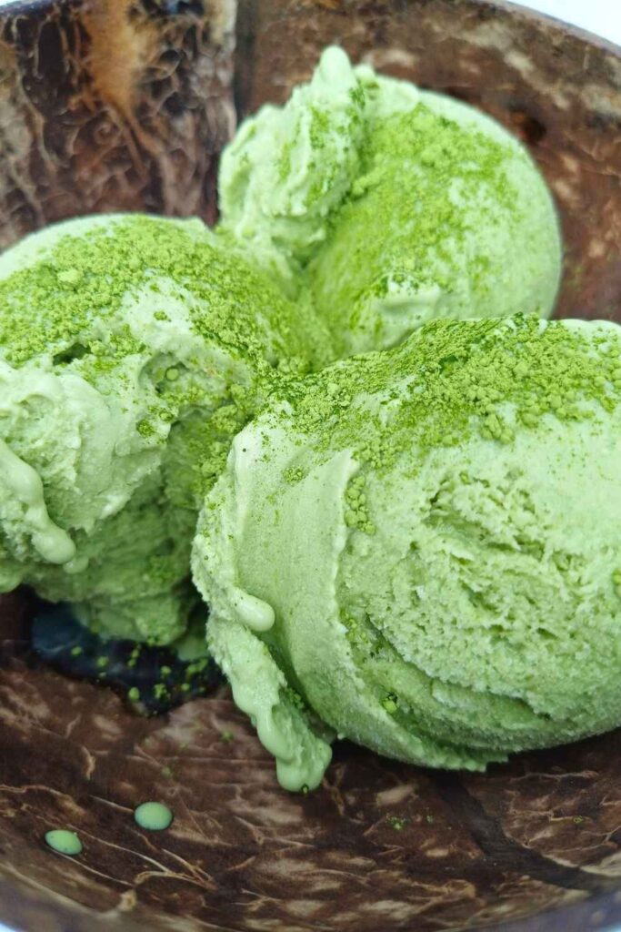 Three scoops of vibrant green matcha flavored ice cream in a coconut shell bowl
