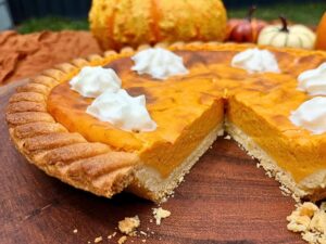 A pumpkin pie close up with a piece cut out to show the inside of the pie with dollops of whipped cream on top