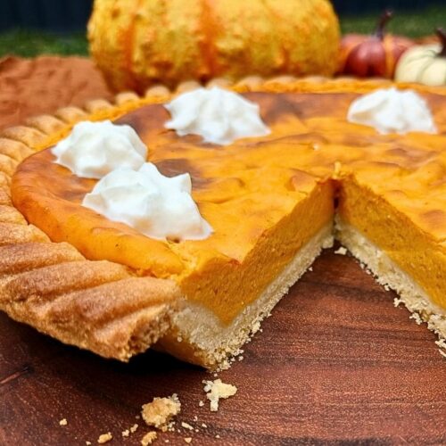 A pumpkin pie close up with a piece cut out to show the inside of the pie with dollops of whipped cream on top