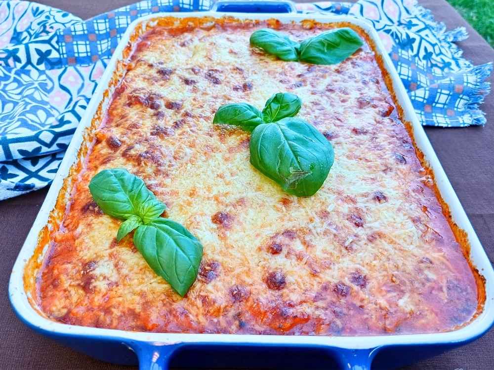 A freshly baked casserole with chicken and cauliflower inside in a tomato sauce with melted cheese on top and fresh herbs for garnish.