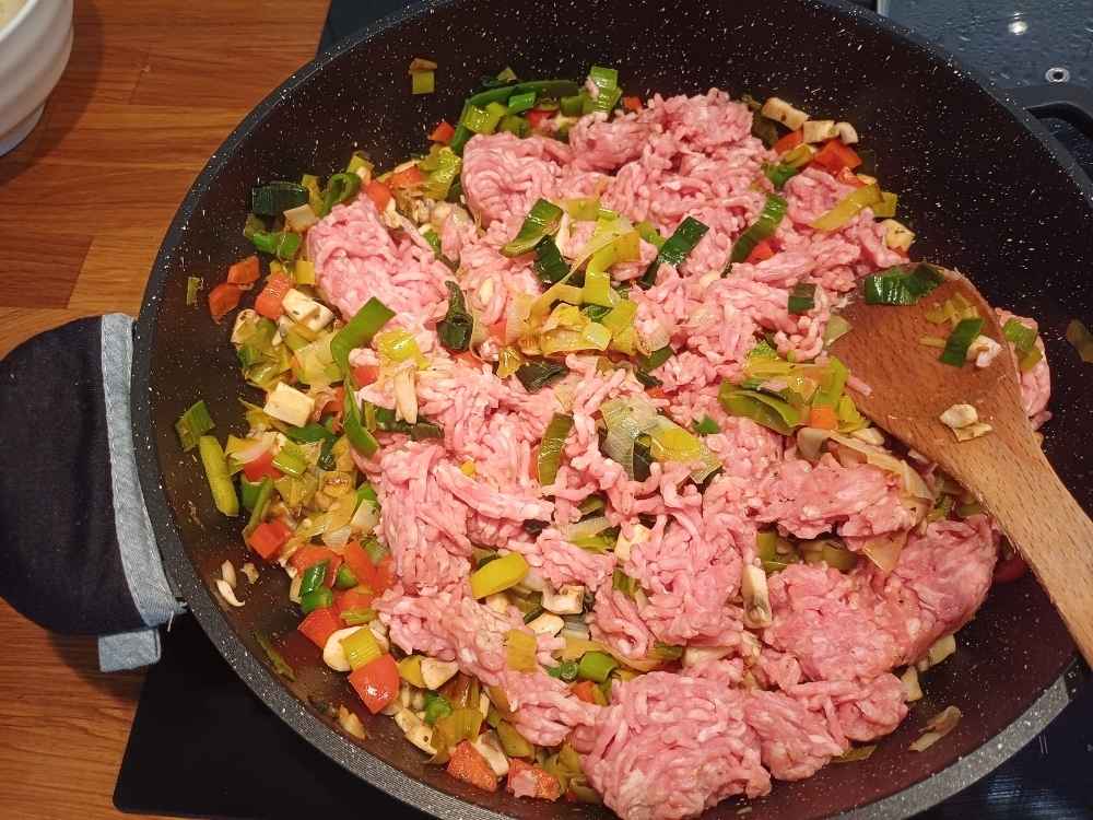Ground pork added to the sautee vegetables on a frying pan