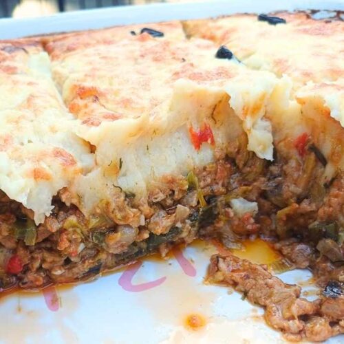 A casserole in a baking dish with one pice cut out to show the inside layers of the casserole