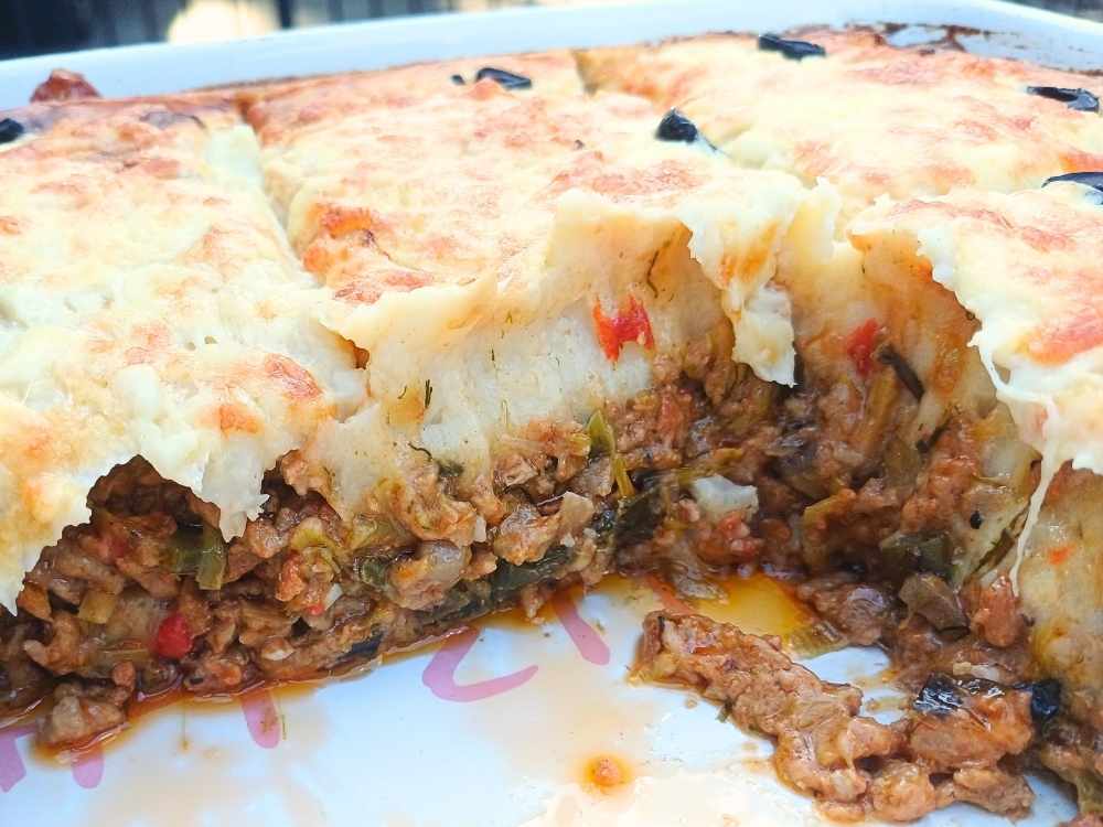 A casserole in a baking dish with one pice cut out to show the inside layers of the casserole