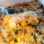 Close up view of a keto butternut squash casserole with spinach and zucchini on a serving spoon