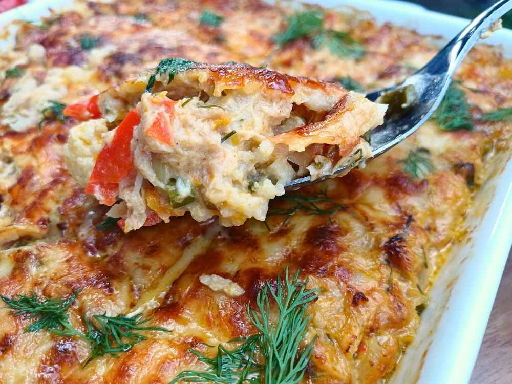 A spoon lifting a mouthful of keto tuna casserole from the baking tray to show the inside of the dish