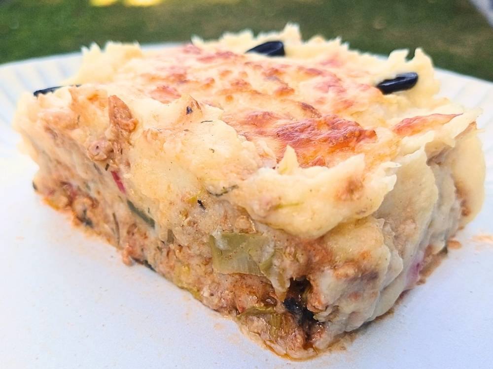 A slice of low carb casserole showing layers of cooked ground pork with vegetables and cheesy sauce