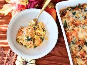 A view of fall theme styled keto butternut squash casserole serving in a bowl with small pumpkins and maple leaves around on orange cloth