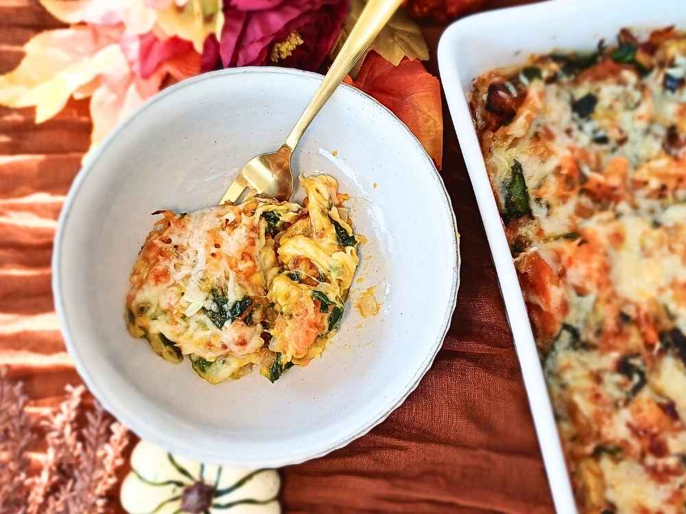 A view of fall theme styled keto butternut squash casserole serving in a bowl with small pumpkins and maple leaves around on orange cloth