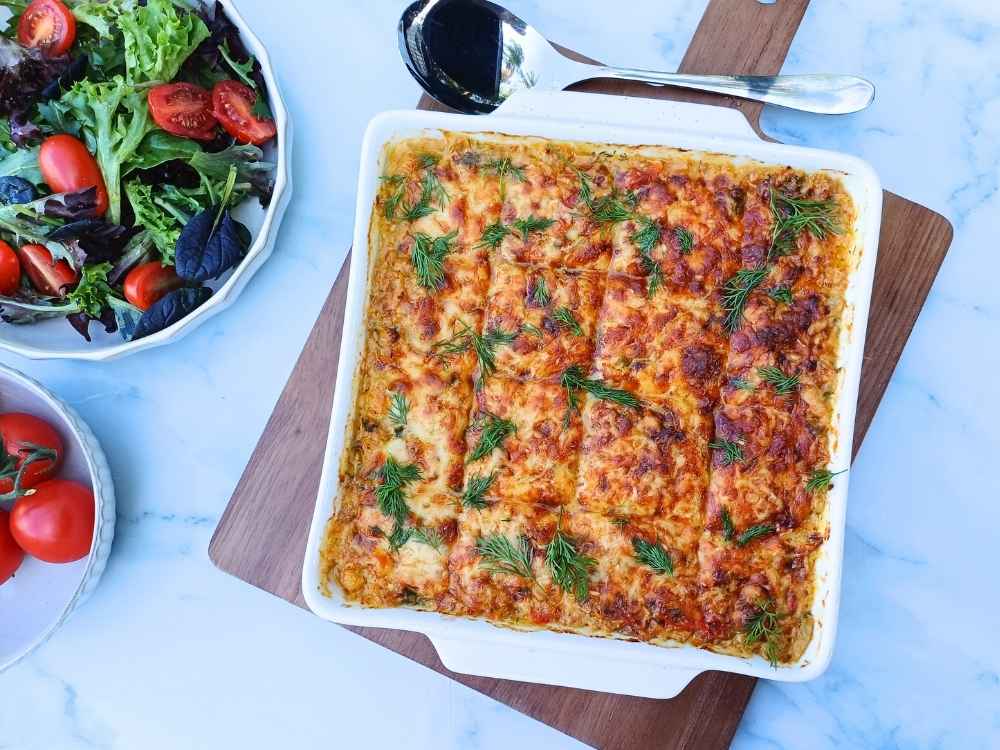 Top down view of a square baking dish filled with golden cheesy keto tuna casserole and some side salad on the table