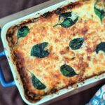 Golden cheesy casserole in a blue baking dish, decorated with spinach leaves.