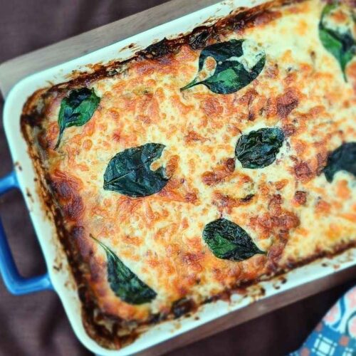 Golden cheesy casserole in a blue baking dish, decorated with spinach leaves.