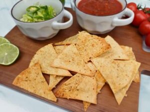 Keto tortilla chips on a wooden board with guacamole and salasa in the background
