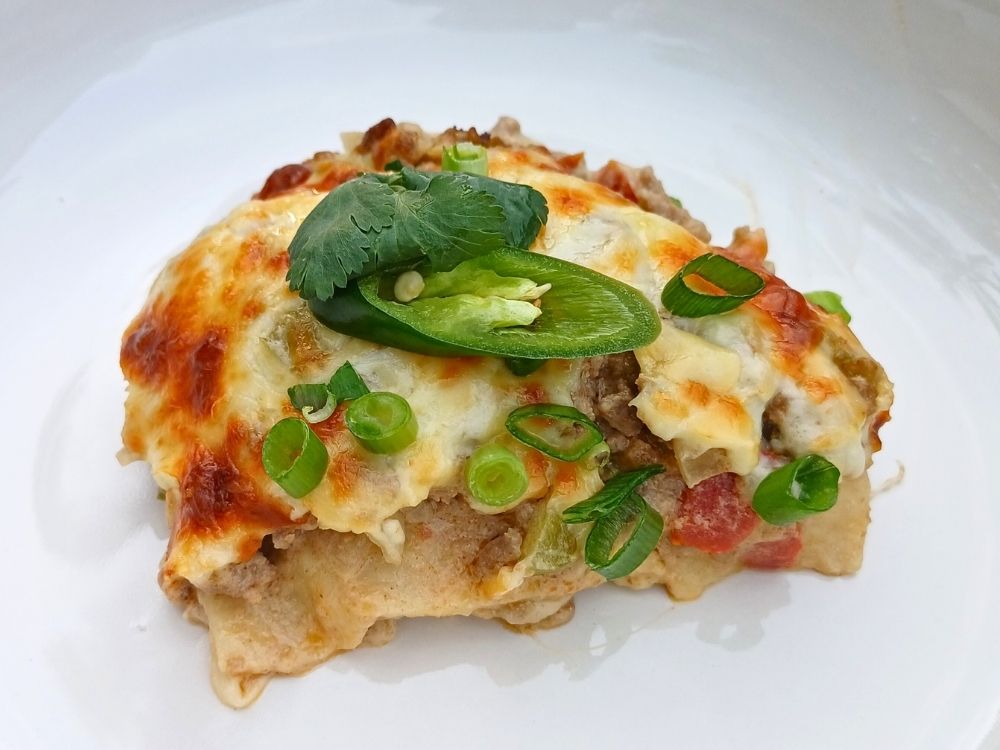 A protion of a keto taco casserole on a whte plate topped with fresh cilantro, green onions and green chilis