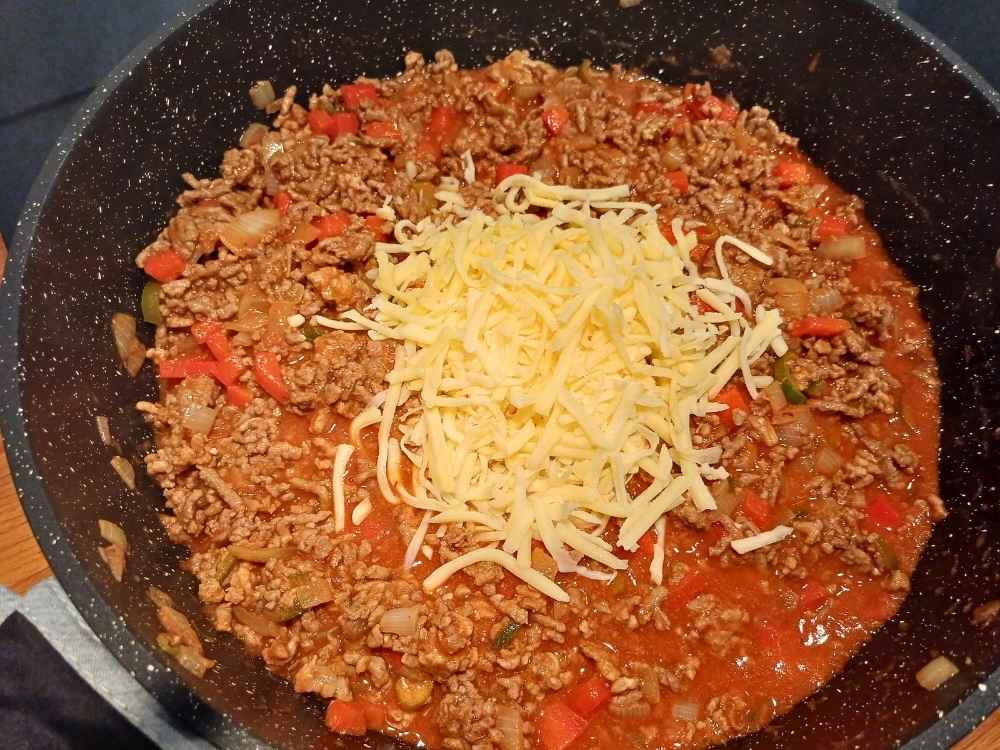 Shredded mexican cheese being added to the ground beef mixture while on the stove top cooking