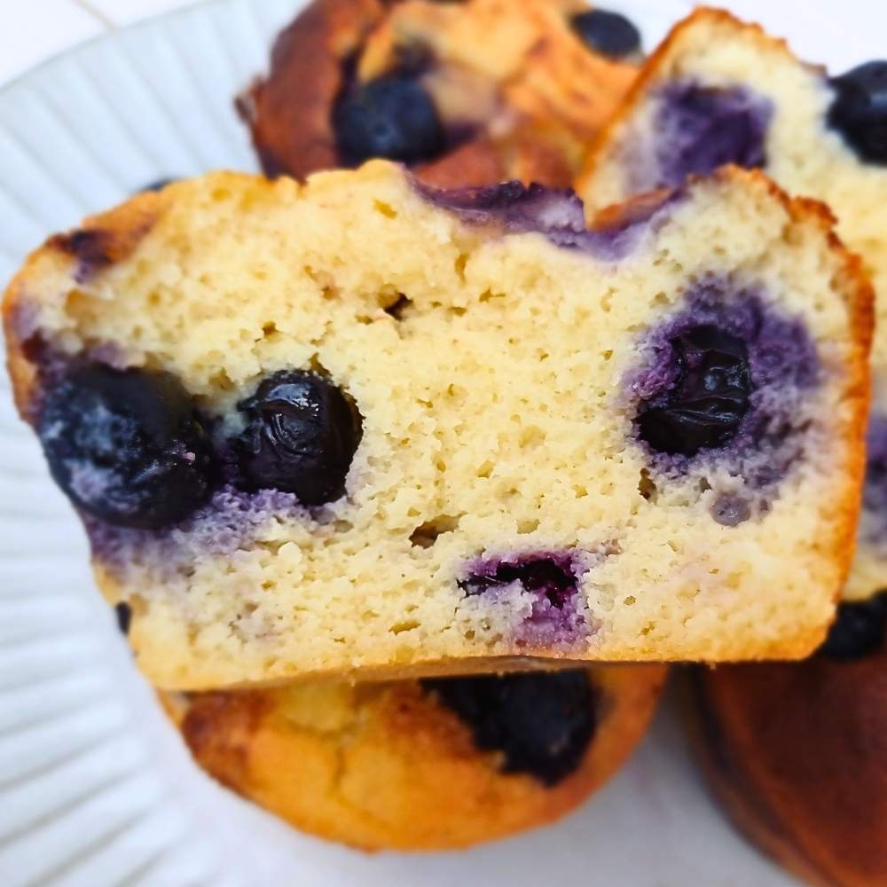 An open almond flour blueberry muffin showing soft flurry inside with juicy blueberries