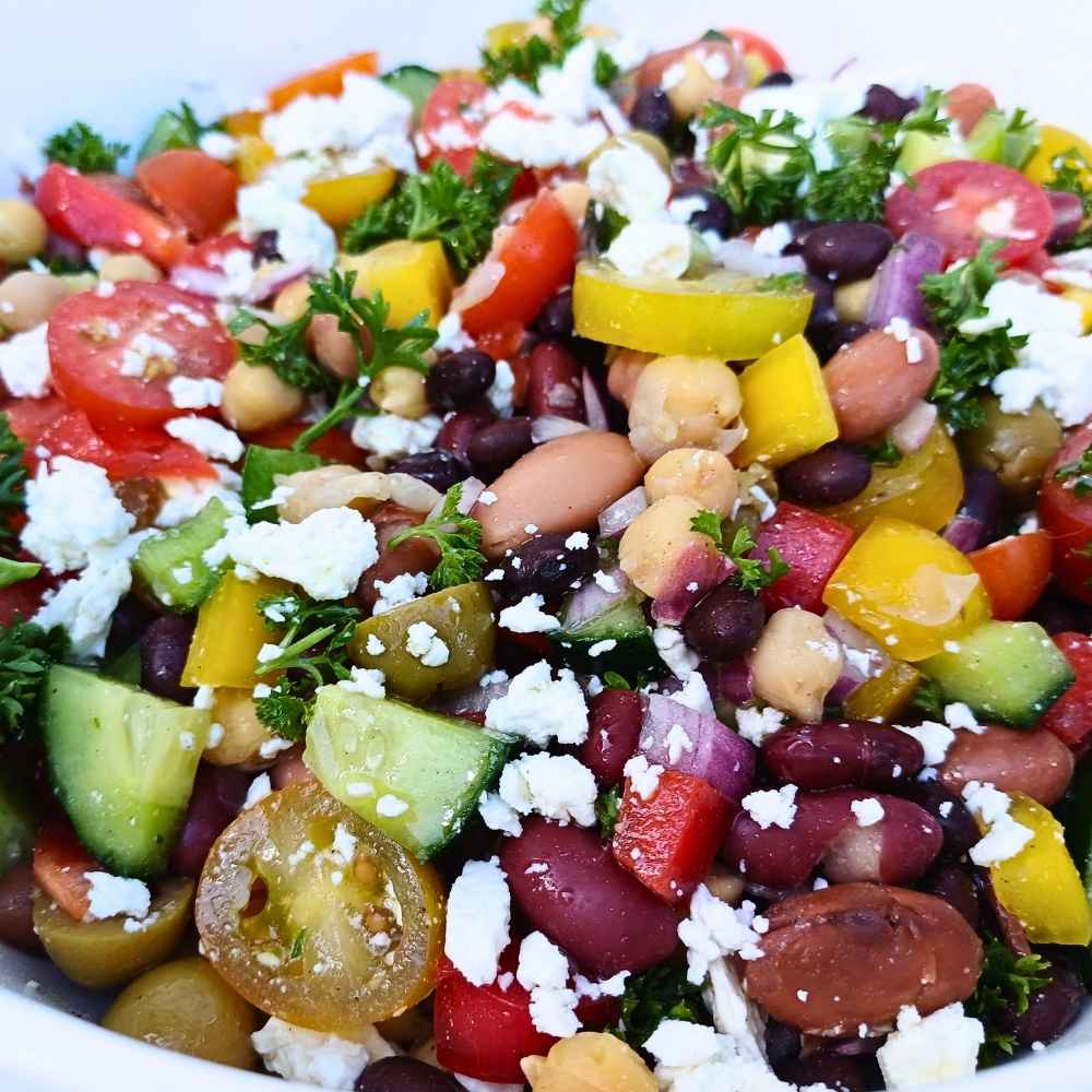 A close up shot of a dense bean salad with vegetables and feta