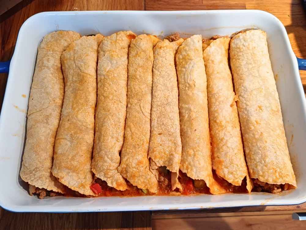 Eight enchiladas stacked together in a baking tray without sauce