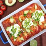 Top down view of a keto beef enchilada casserole topped with sour cream and fresh herbs other vegetables ont he side for decoration