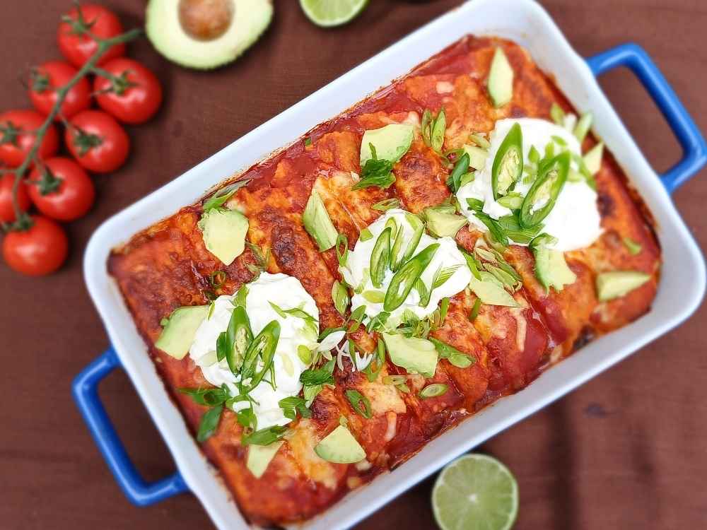 Top down view of a baking dish filled with keto beef enchilada casserole topped with sour cream and fresh chillis
