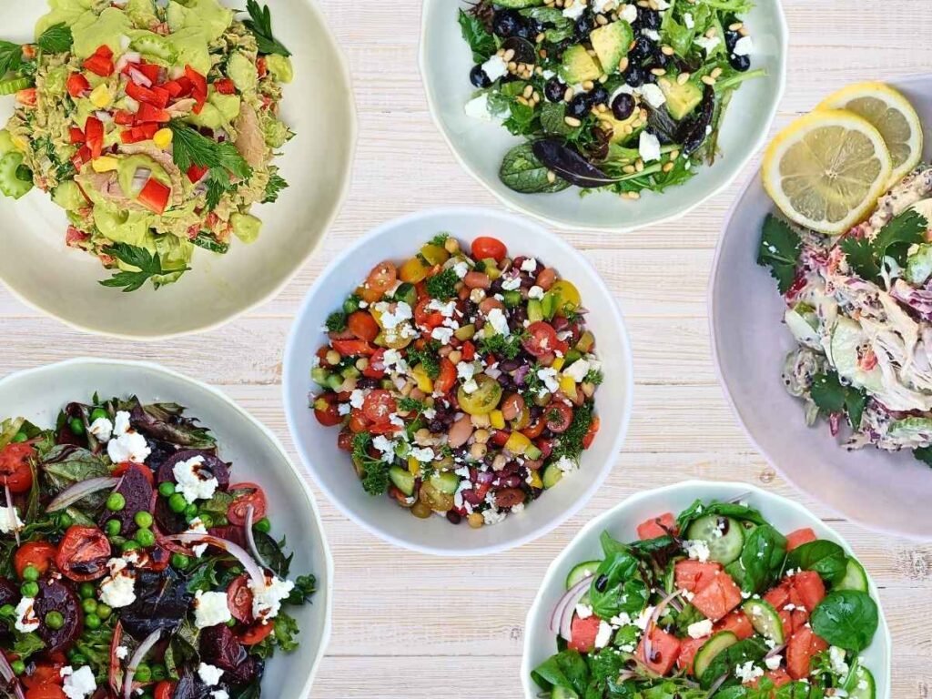 bowls of healthy salads on a wooden light colored table