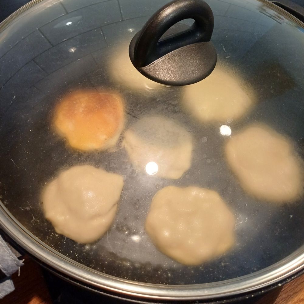 Small pancakes on a frying pan cooking covered with glass lid