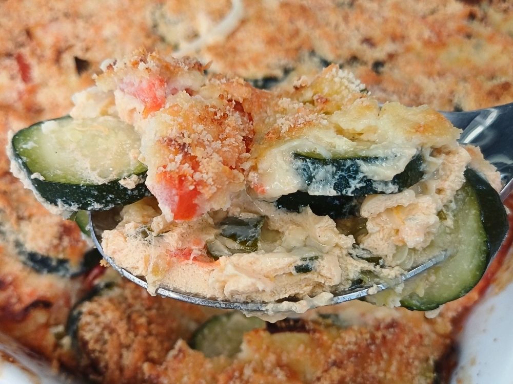Close up of a zucchini and tomato bake in cheesy sauce on a spoon.