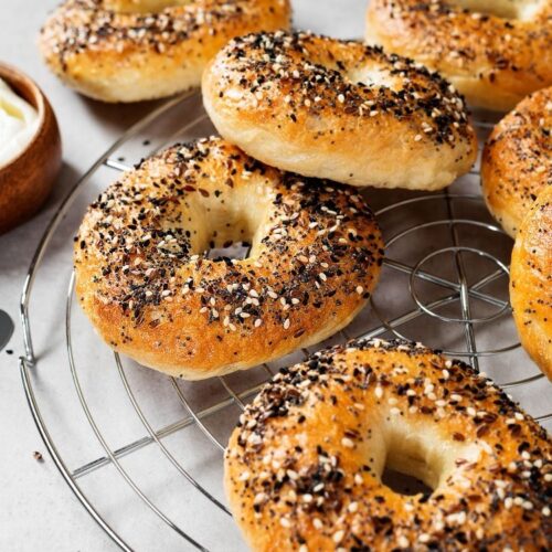 A few sourdough bagels with everything seasoning bagels are cooling on a metal rack