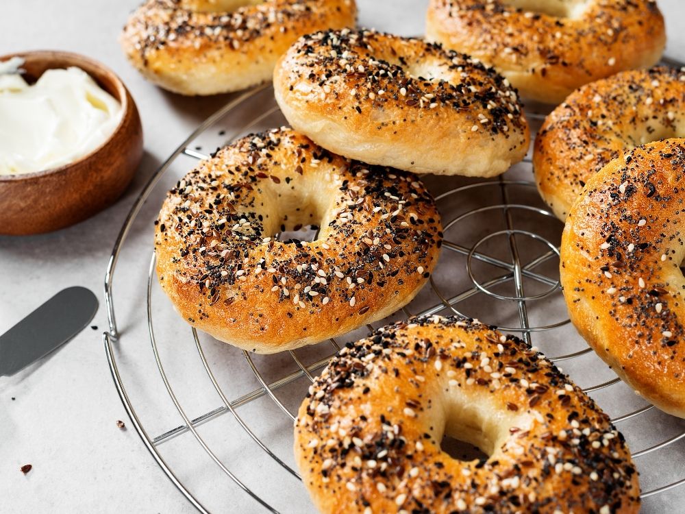 A few sourdough bagels with everything seasoning bagels are cooling on a metal rack