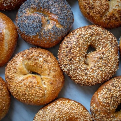 Freshly baked sourdough bagels layed out on parchment paper sprinckled with seasame seeds, poppy seeds and everything seasoning