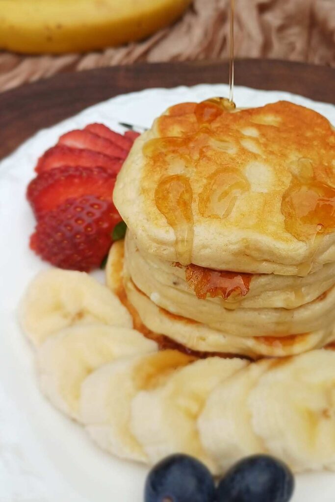 Stack of small pancakes on a white plate with some fruit on the side
