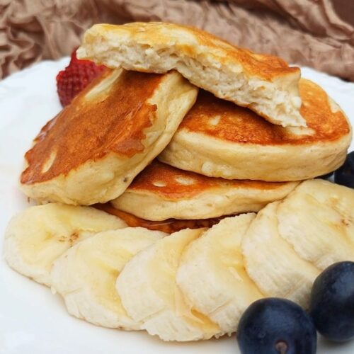 Stack of fluffy gluten free cottage cheese pancakes with one broken open to show the inside.