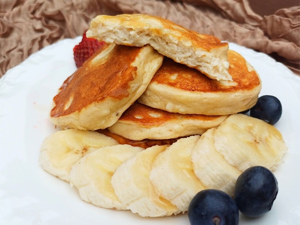 Stack of fluffy gluten free cottage cheese pancakes with one broken open to show the inside.