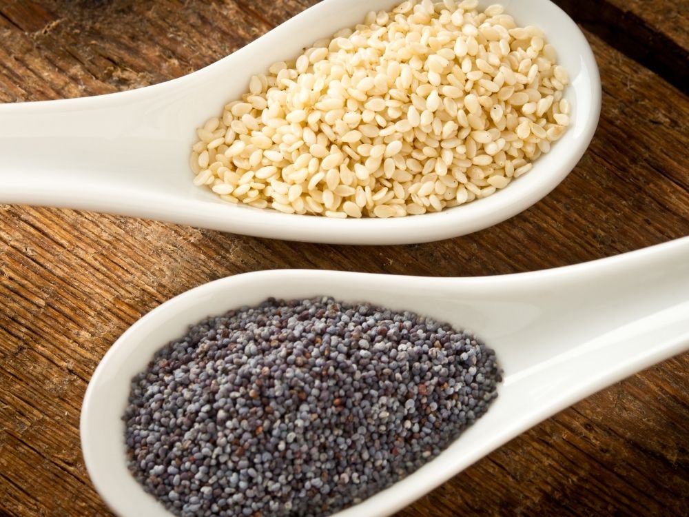 White seasame seeds and black poppy seeds on separate ceramic white spoons