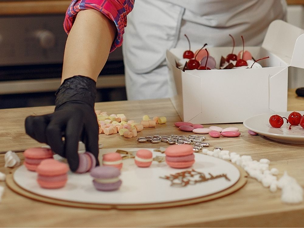 Womans hand assembling desserts on a charcuterie board and platters wearing black latex glove.