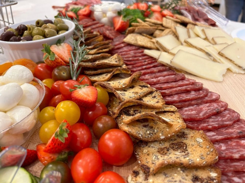A close up angle view of summer charcuterie board items like salami, crackers, cherry tomatos and mozarella balls.