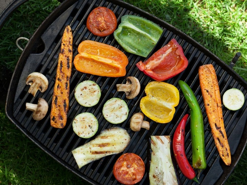 Vegetables layed out on a grill including zucchini, peppers, carots and mushrooms.