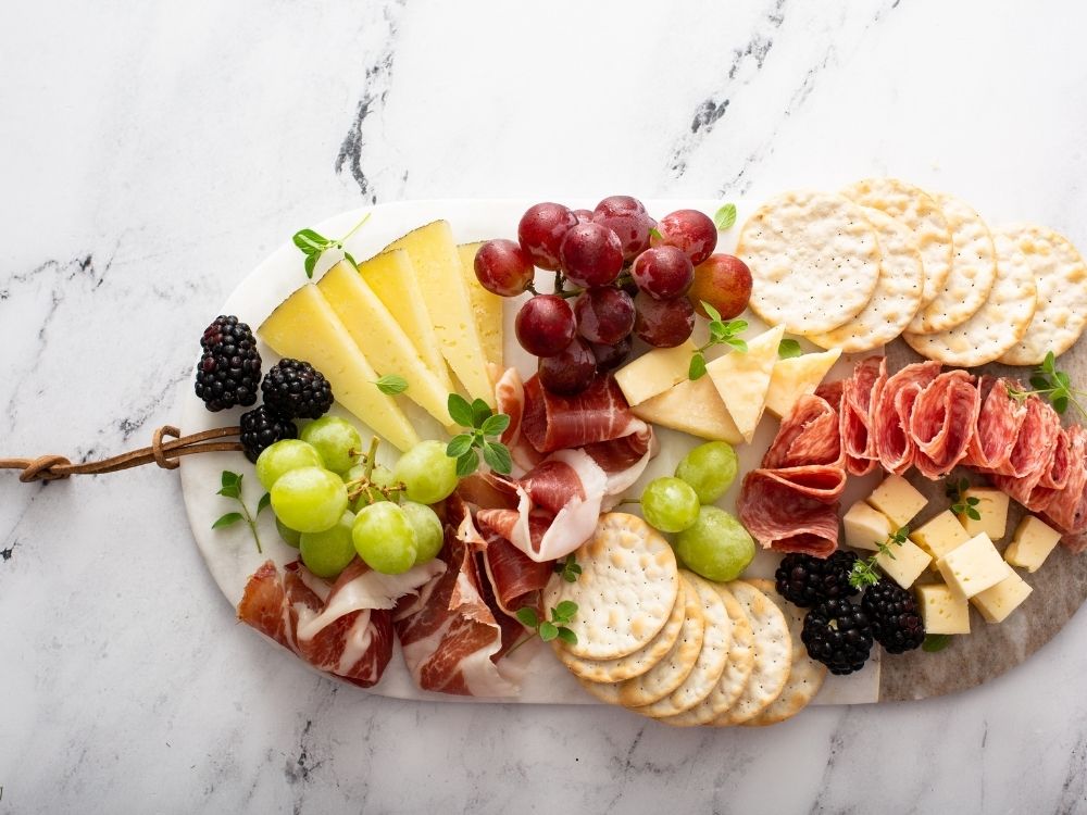 Oval oblong charcuterie board filled with grapes, crackers, cheese cubes, cured meats and blackberries.