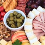 Close up of a simple charuterie board with ham, cheeses, slami, olives and fruits.