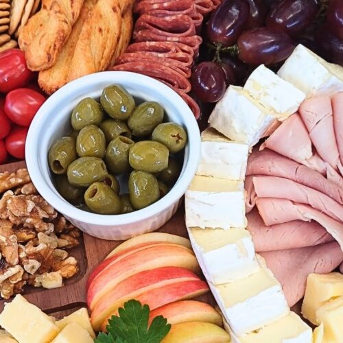 Close up of a simple charuterie board with ham, cheeses, slami, olives and fruits.