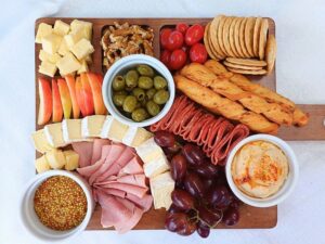 Top down view of a simple charcuterie board with ham, salami, crackers, cheeses, wallnuts, olives and hummus.