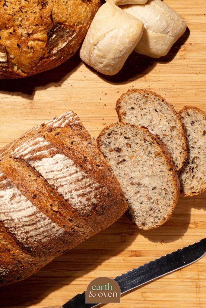 Fresly baked loaf of sourdough discard bread half sliced on a wooden chopping board