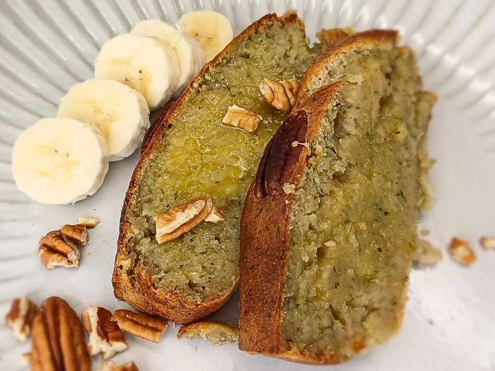 Close up of a banana zucchini bread slices with some banana by the side on a plate.