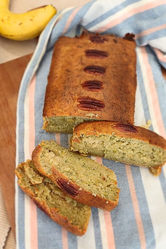 Zucchini banana bread loaf from the top, some of it is sliced on a towel and wooden board.