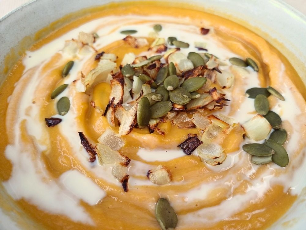 Close up view of a butternut squash soup with caramelized onions and pumpkin seeds on top.